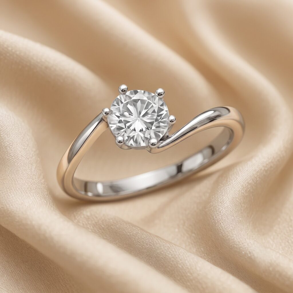 Detaillierte Nahaufnahme eines Solitär-Verlobungsrings aus Weißgold, der auf einem drapierten, champagnerfarbenen Satin-Stoff ruht. Der Ring verfügt über einen asymmetrischen, geschwungenen Bypass-Schaft, der einen großen, runden Brillant-Diamanten hält. Der Diamant ist in einer Sechser-Krappenfassung sicher gefasst. Der Hintergrund zeigt weiche, fließende Falten des glänzenden Stoffes mit subtilem Glanz. Die Beleuchtung ist weich und diffus.